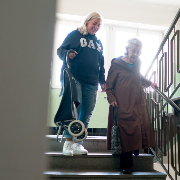 Caregiver helps senior woman navigate stairs indoors, emphasizing elderly care and support.