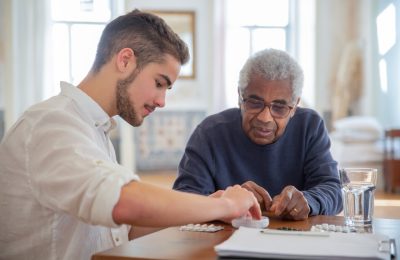 A young volunteer helps an elderly man manage his medication at a nursing home.