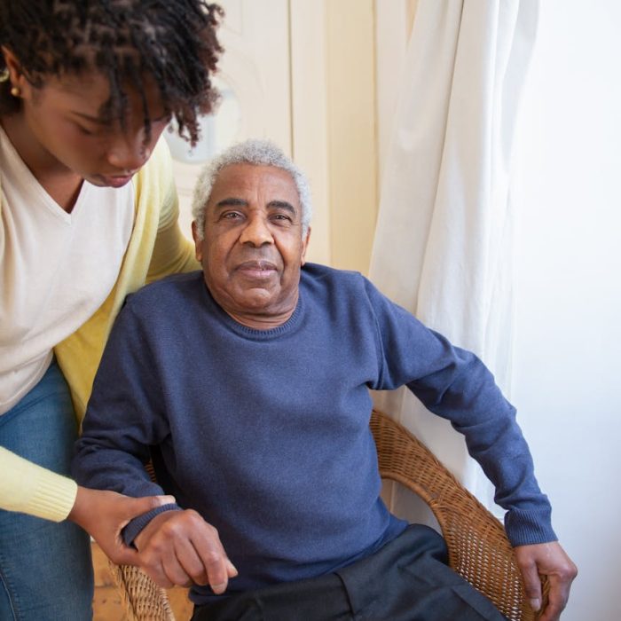 A woman assists an elderly man indoors, focusing on care and support.